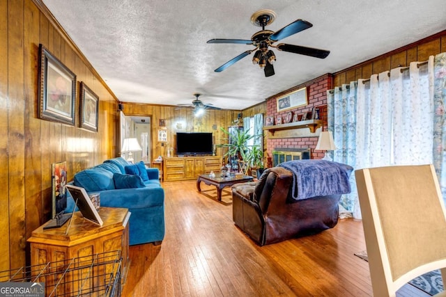 living room featuring wooden walls, a fireplace, wood-type flooring, crown molding, and a textured ceiling