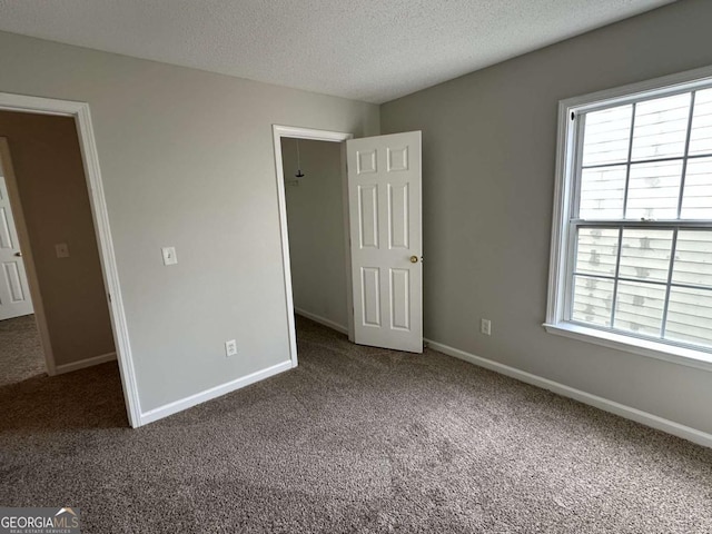 unfurnished bedroom featuring dark colored carpet, a spacious closet, and a textured ceiling