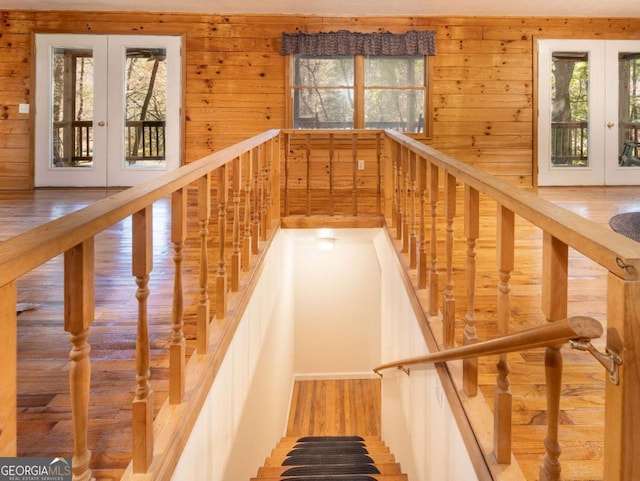 stairs featuring french doors, wood-type flooring, and wooden walls