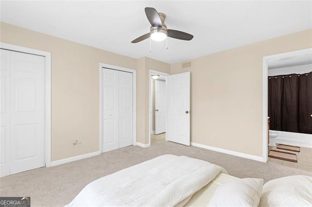 carpeted bedroom featuring connected bathroom, two closets, and ceiling fan