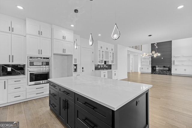 kitchen featuring white cabinetry, hanging light fixtures, a center island, stainless steel double oven, and light hardwood / wood-style flooring