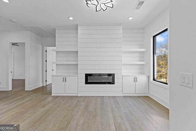 unfurnished living room featuring a large fireplace, heating unit, and light hardwood / wood-style flooring