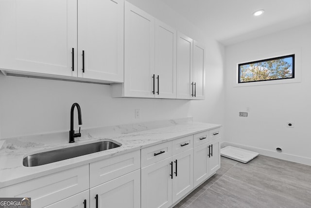 kitchen with white cabinetry, light stone countertops, and sink