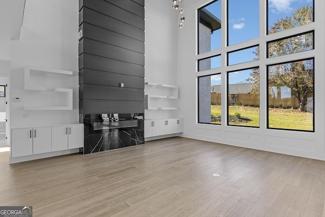 unfurnished living room with a towering ceiling, plenty of natural light, and light hardwood / wood-style floors