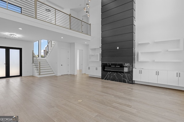 unfurnished living room with a towering ceiling, a fireplace, light wood-type flooring, and french doors