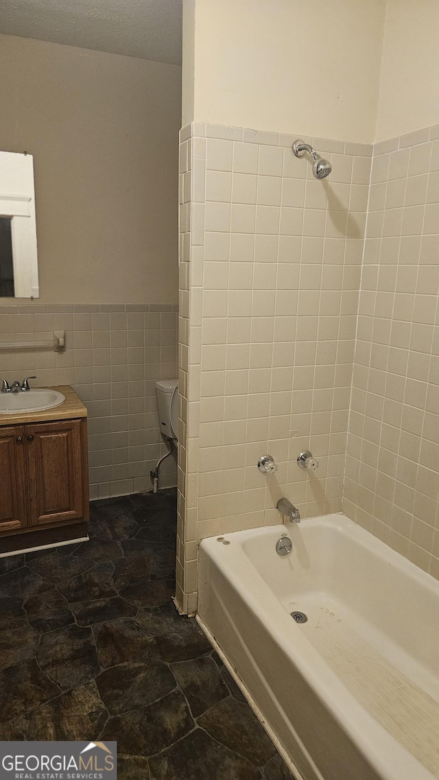 full bathroom with tiled shower / bath, vanity, toilet, and tile walls