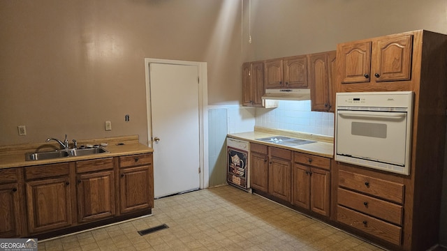 kitchen with sink, a towering ceiling, oven, black electric stovetop, and beverage cooler