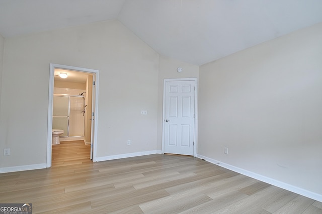 unfurnished bedroom featuring vaulted ceiling, ensuite bathroom, and light wood-type flooring