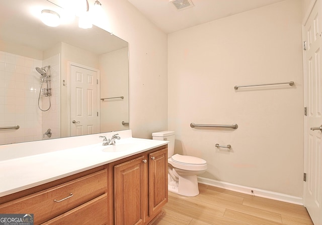 bathroom with vanity, toilet, hardwood / wood-style floors, and a tile shower