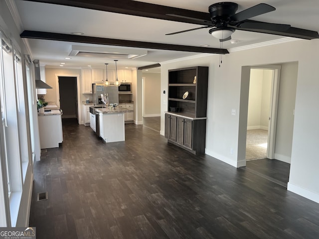 kitchen featuring beamed ceiling, an island with sink, pendant lighting, stainless steel appliances, and white cabinets