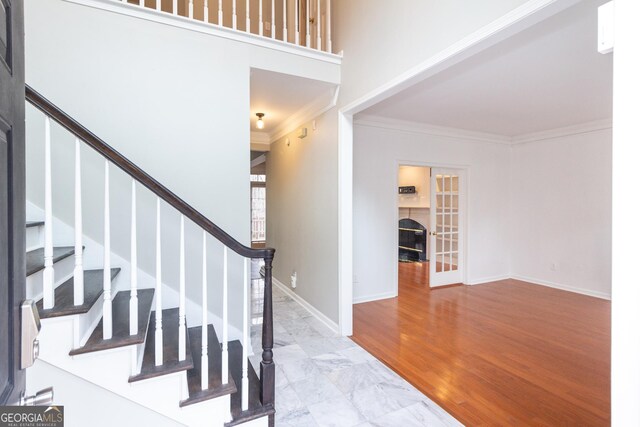 stairway with hardwood / wood-style floors, a towering ceiling, and ornamental molding