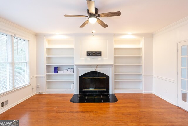 unfurnished living room with a fireplace, hardwood / wood-style flooring, ornamental molding, ceiling fan, and built in shelves