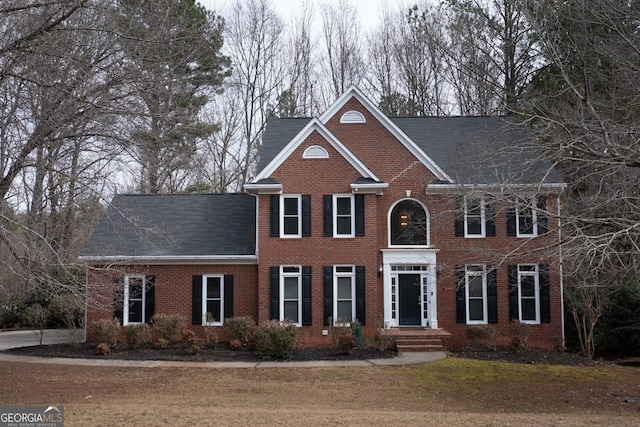 colonial home featuring brick siding, a shingled roof, and a front yard