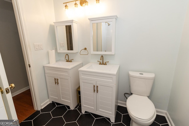 bathroom with a sink, baseboards, toilet, and two vanities