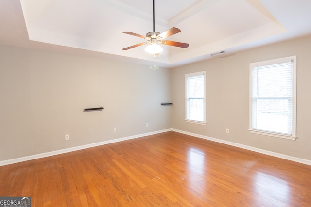 unfurnished room featuring visible vents, ceiling fan, baseboards, light wood-style floors, and a raised ceiling