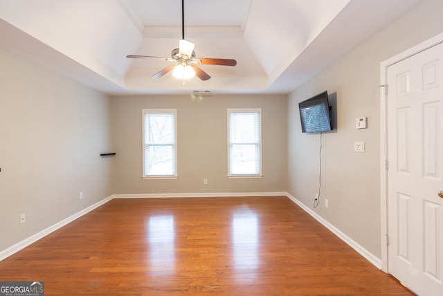 unfurnished room featuring ceiling fan, a raised ceiling, baseboards, and wood finished floors