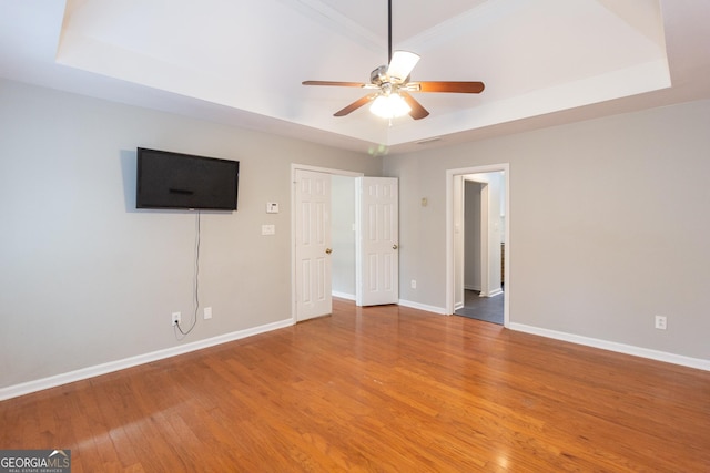 unfurnished bedroom with a ceiling fan, a tray ceiling, light wood-style floors, and baseboards