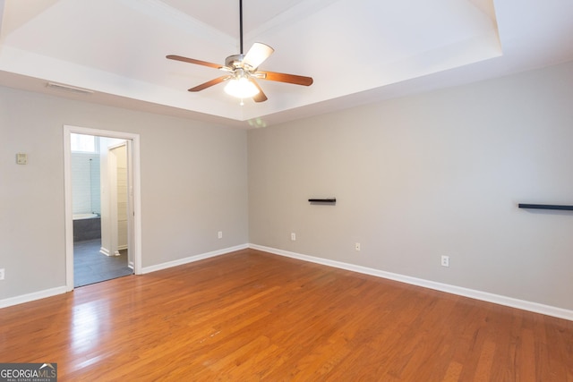 spare room featuring a ceiling fan, visible vents, baseboards, a tray ceiling, and light wood-type flooring