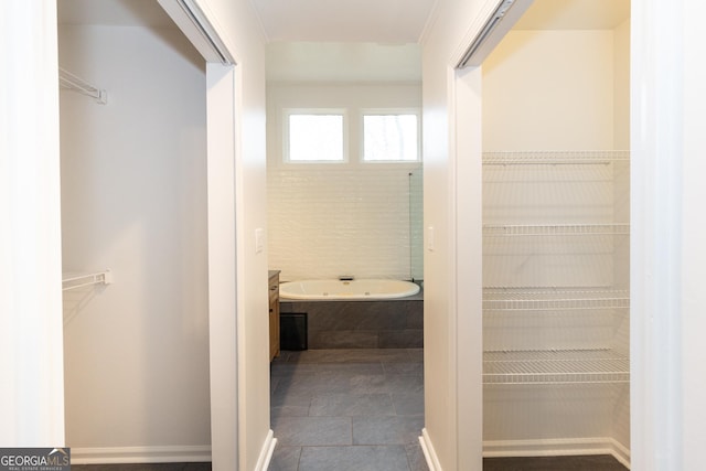 bathroom with a walk in closet, a garden tub, and vanity