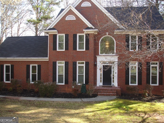 view of front of house with brick siding, a front yard, and roof with shingles