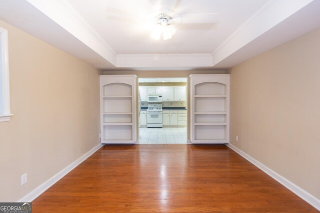 empty room with crown molding, ceiling fan, a tray ceiling, wood-type flooring, and french doors