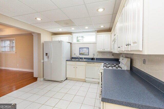 kitchen featuring white cabinetry, sink, backsplash, light tile patterned floors, and white appliances