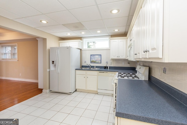 kitchen featuring white appliances, a sink, white cabinets, dark countertops, and backsplash