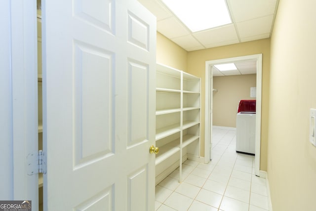 hallway with washer / dryer, light tile patterned flooring, a paneled ceiling, and baseboards