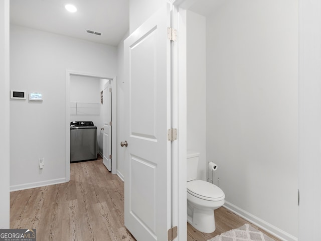 bathroom with toilet, wood-type flooring, and washer / clothes dryer