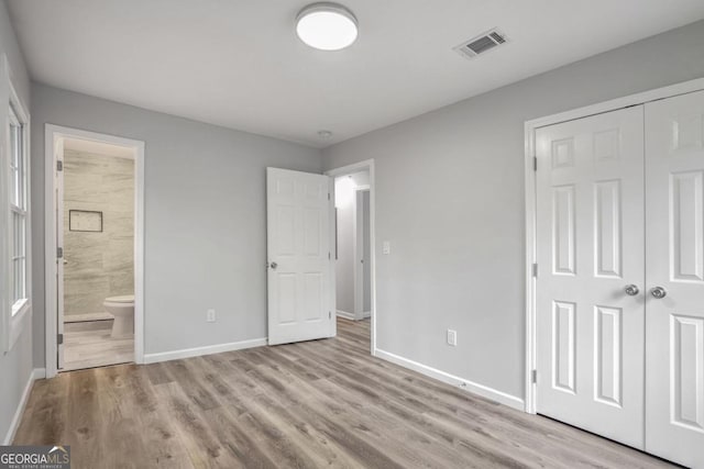 unfurnished bedroom featuring ensuite bath, a closet, and light wood-type flooring