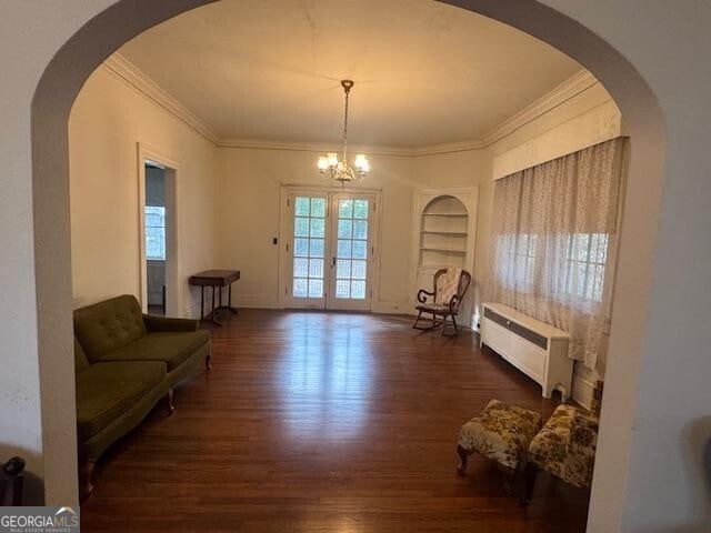 living area with radiator, crown molding, an inviting chandelier, dark hardwood / wood-style floors, and built in shelves