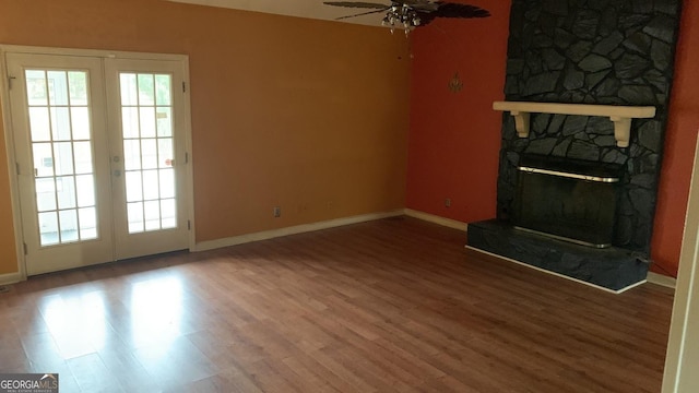 unfurnished living room featuring hardwood / wood-style flooring, a stone fireplace, ceiling fan, and french doors