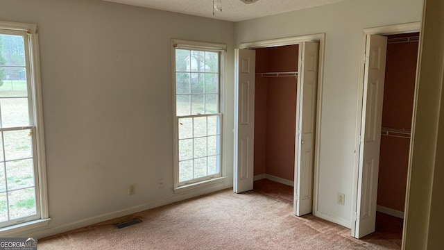 unfurnished bedroom with light carpet, multiple windows, and a textured ceiling