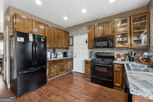 kitchen featuring sink, light stone counters, black appliances, dark hardwood / wood-style floors, and backsplash