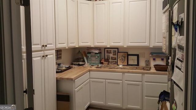 kitchen with wood counters, refrigerator, and white cabinets