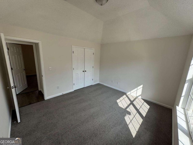 unfurnished bedroom featuring vaulted ceiling, a closet, a textured ceiling, and dark colored carpet