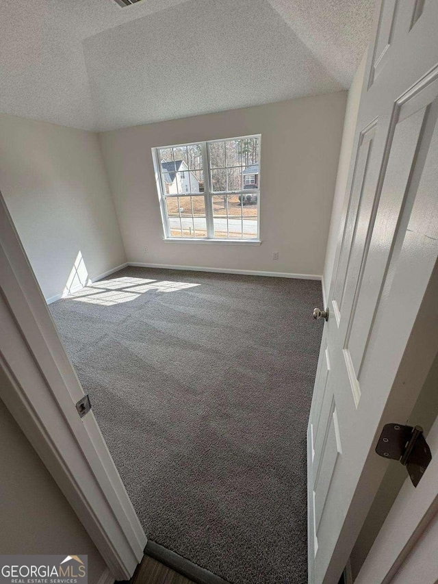 carpeted spare room with vaulted ceiling and a textured ceiling