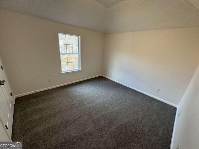 spare room with dark carpet and vaulted ceiling