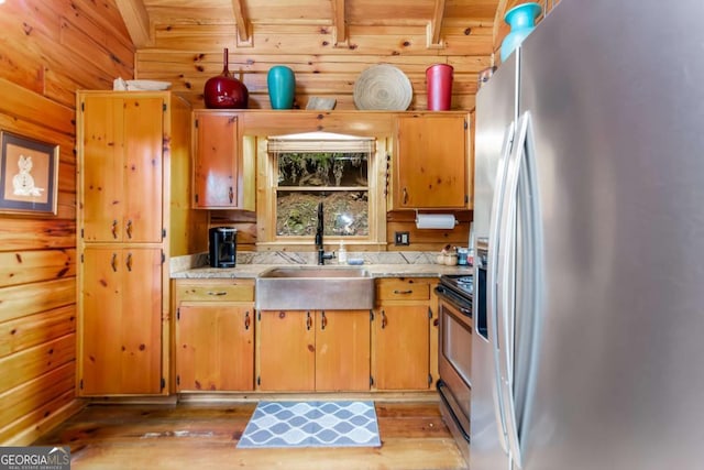 kitchen with sink, appliances with stainless steel finishes, wooden walls, light stone countertops, and light hardwood / wood-style floors