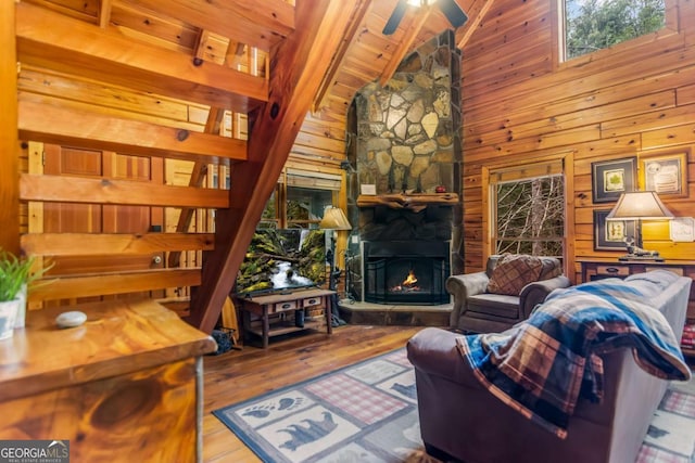 living room featuring hardwood / wood-style floors, high vaulted ceiling, a fireplace, wood walls, and ceiling fan