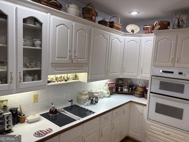 kitchen with black electric cooktop, white cabinets, white double oven, and decorative backsplash