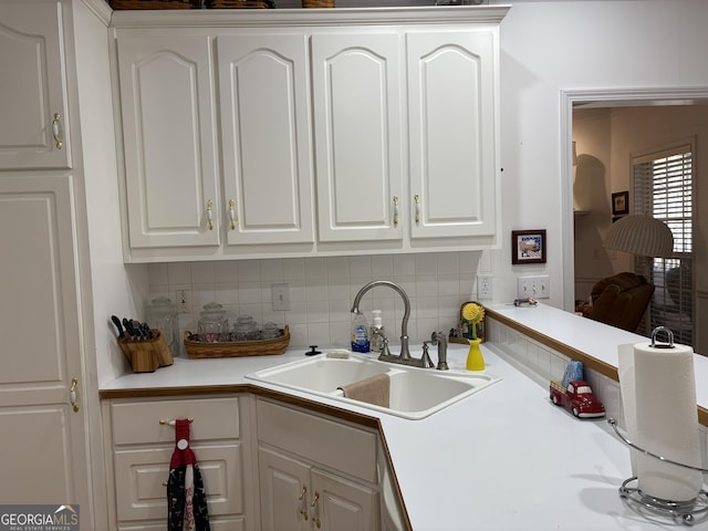 kitchen with white cabinetry, light countertops, backsplash, and a sink