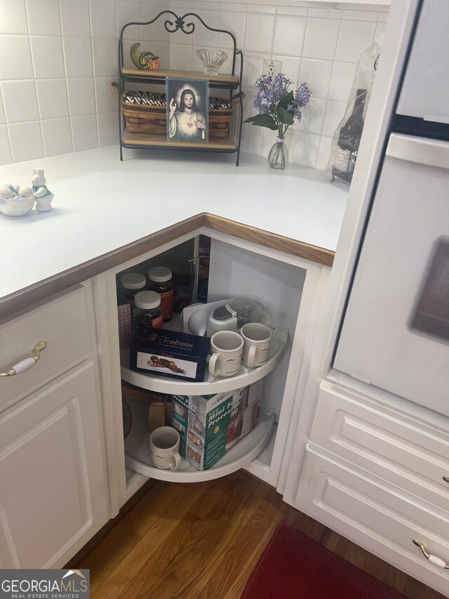 details featuring tasteful backsplash, dark wood finished floors, white cabinets, and light countertops