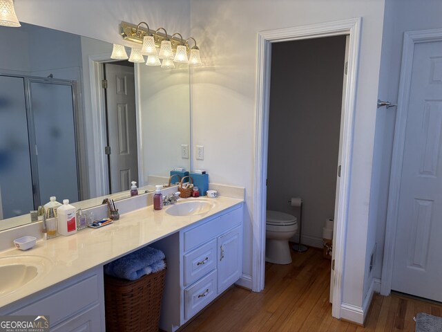 full bathroom featuring wood finished floors, double vanity, a stall shower, a sink, and toilet