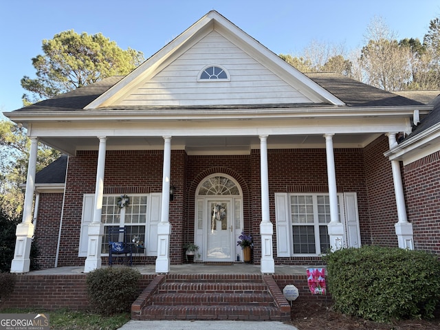 view of front facade with brick siding, a porch, and roof with shingles