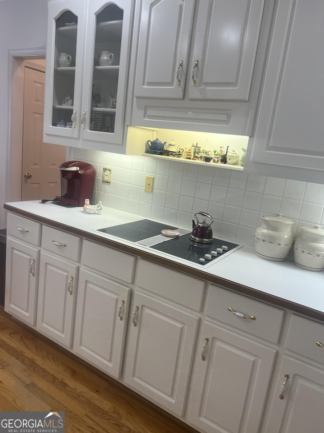 kitchen featuring decorative backsplash, white cabinets, light countertops, and glass insert cabinets