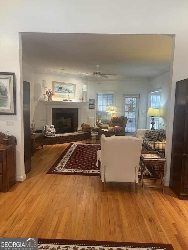 living area with light wood finished floors, a brick fireplace, crown molding, and ceiling fan