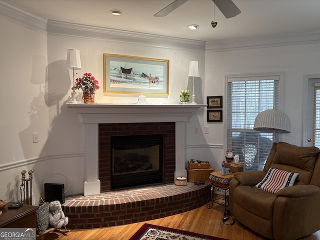 living area featuring a brick fireplace, crown molding, a ceiling fan, and wood finished floors