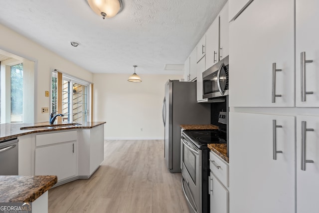 kitchen featuring sink, white cabinetry, decorative light fixtures, stainless steel appliances, and light hardwood / wood-style floors