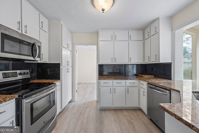 kitchen featuring white cabinetry, stainless steel appliances, and dark stone counters